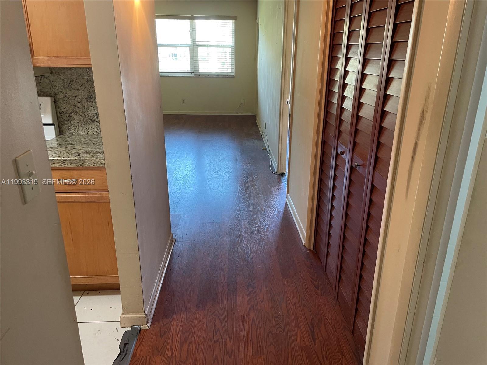 A hallway with dark wood flooring leads to a room with a window and closet — 2300 Park Ln # 208, Hollywood FL 33021, HOLLYWOOD, FL