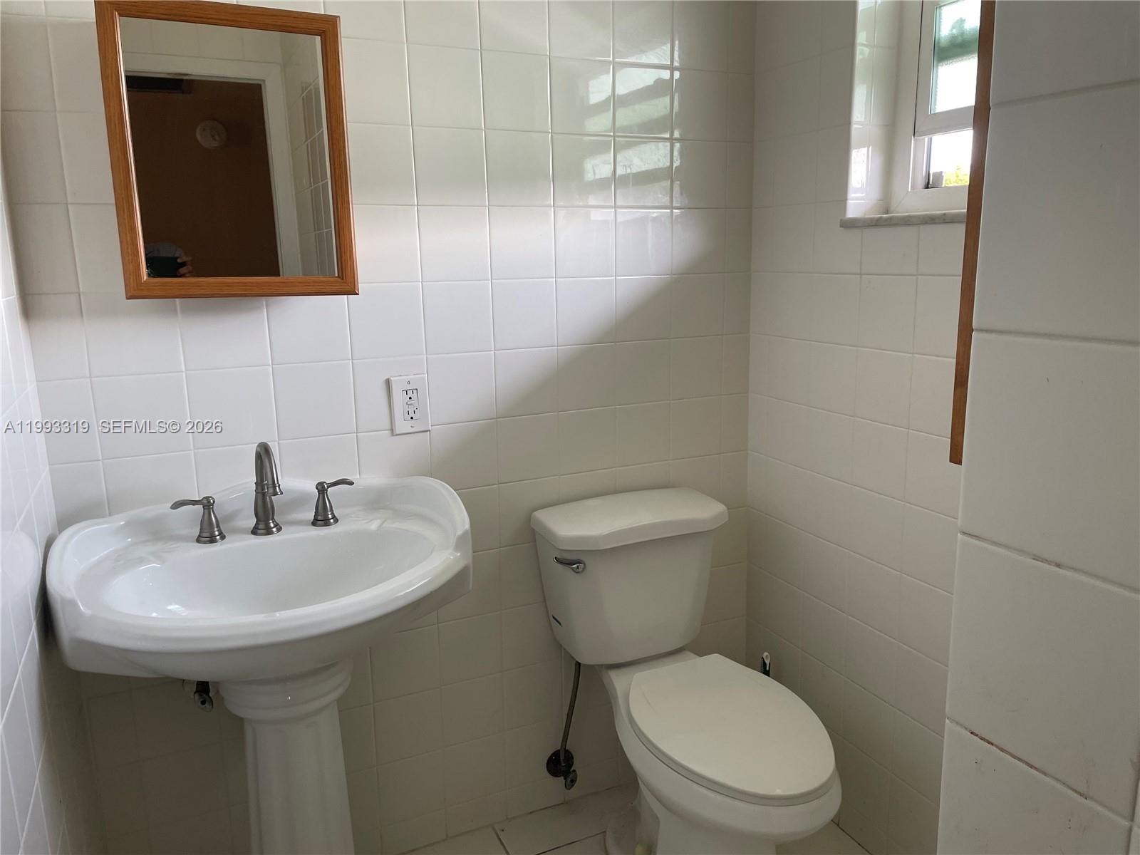 A small bathroom features white wall tiles, a pedestal sink, and a white toilet — 2300 Park Ln # 208, Hollywood FL 33021, HOLLYWOOD, FL