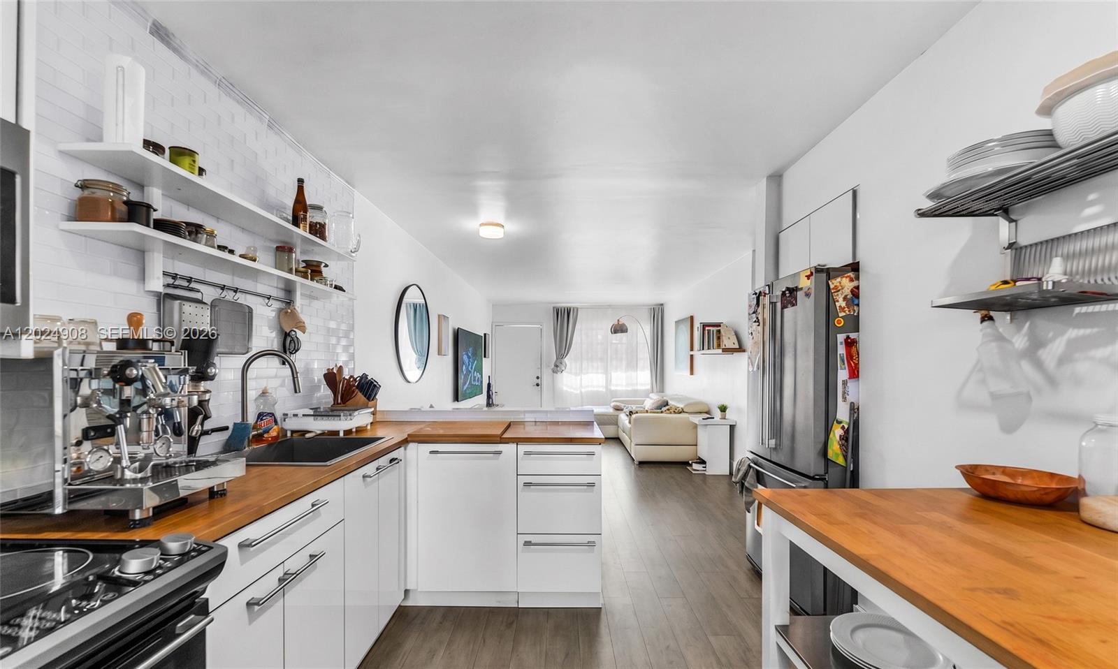 A kitchen with white cabinets, wood countertops, and open shelving opens into a living area — 645 NE 77th St # 1, Miami FL 33138, MIAMI, FL