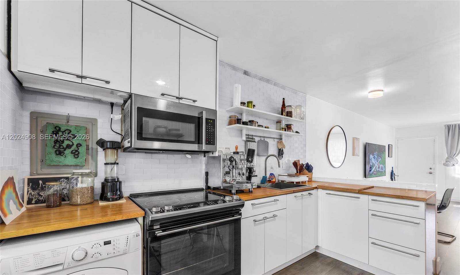 A kitchen features white cabinets, a wood countertop, a built-in microwave, and a washing machine — 645 NE 77th St # 1, Miami FL 33138, MIAMI, FL