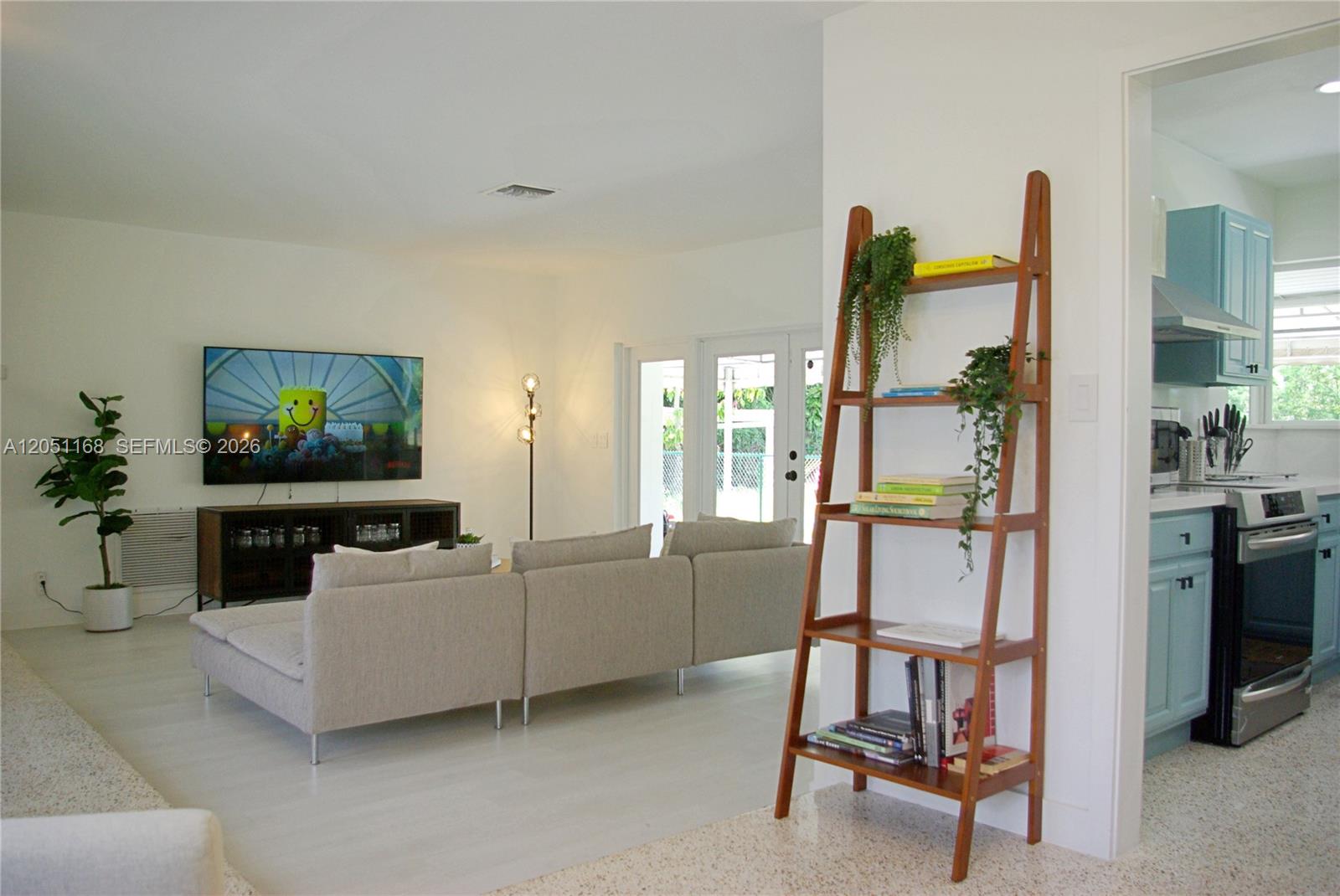 A living room with a sectional sofa, television, and a wooden ladder shelf near a kitchen — 29450 SW 180th Ave, Homestead FL 33030, HOMESTEAD, FL