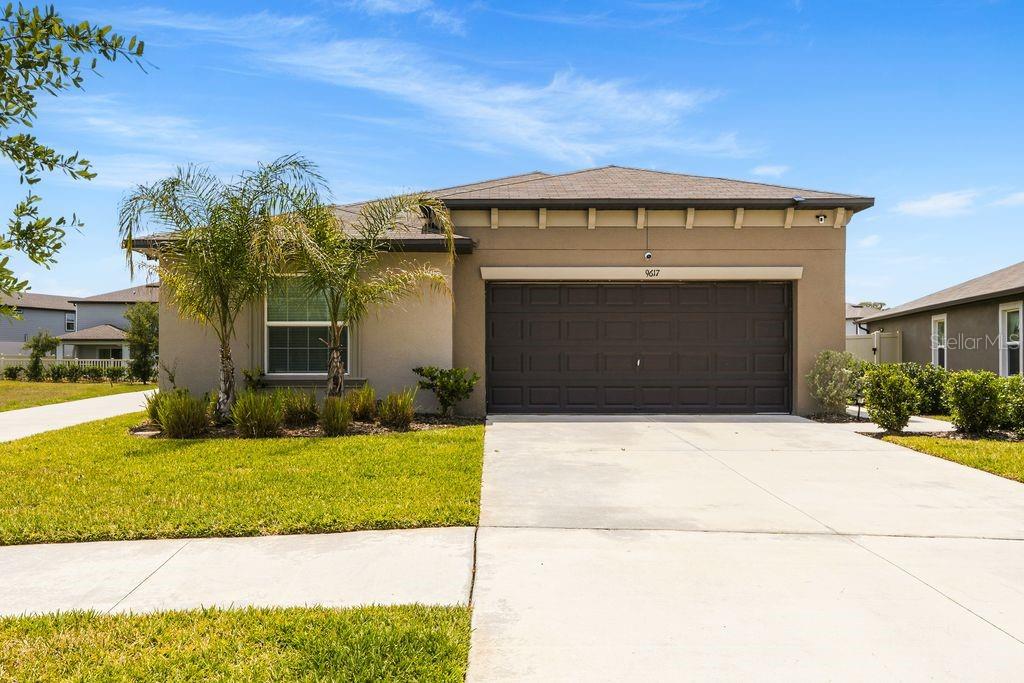A single-story house with a brown exterior, a two-car garage, and a palm tree — 9617 BRANCHING SHIP TRACE, WESLEY CHAPEL, FL