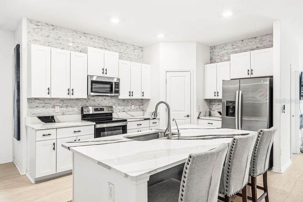 A modern kitchen features white cabinetry, a marble-patterned island, and a stone tile backsplash — 9617 BRANCHING SHIP TRACE, WESLEY CHAPEL, FL