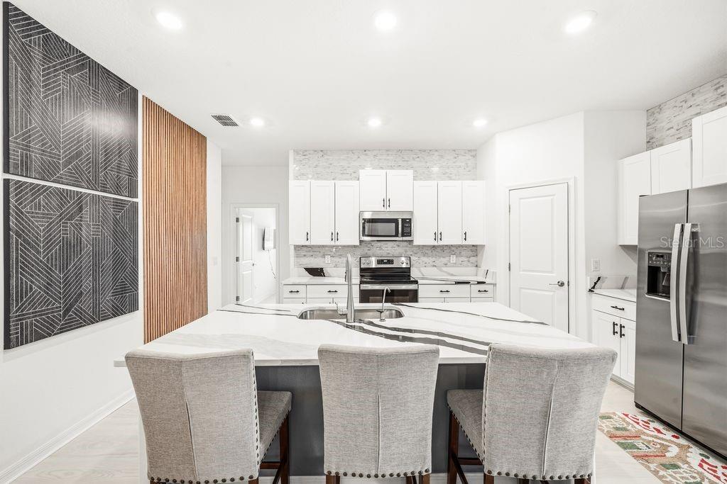 A modern kitchen features a large marble-topped island, white cabinetry, and a wood-slat accent wall — 9617 BRANCHING SHIP TRACE, WESLEY CHAPEL, FL