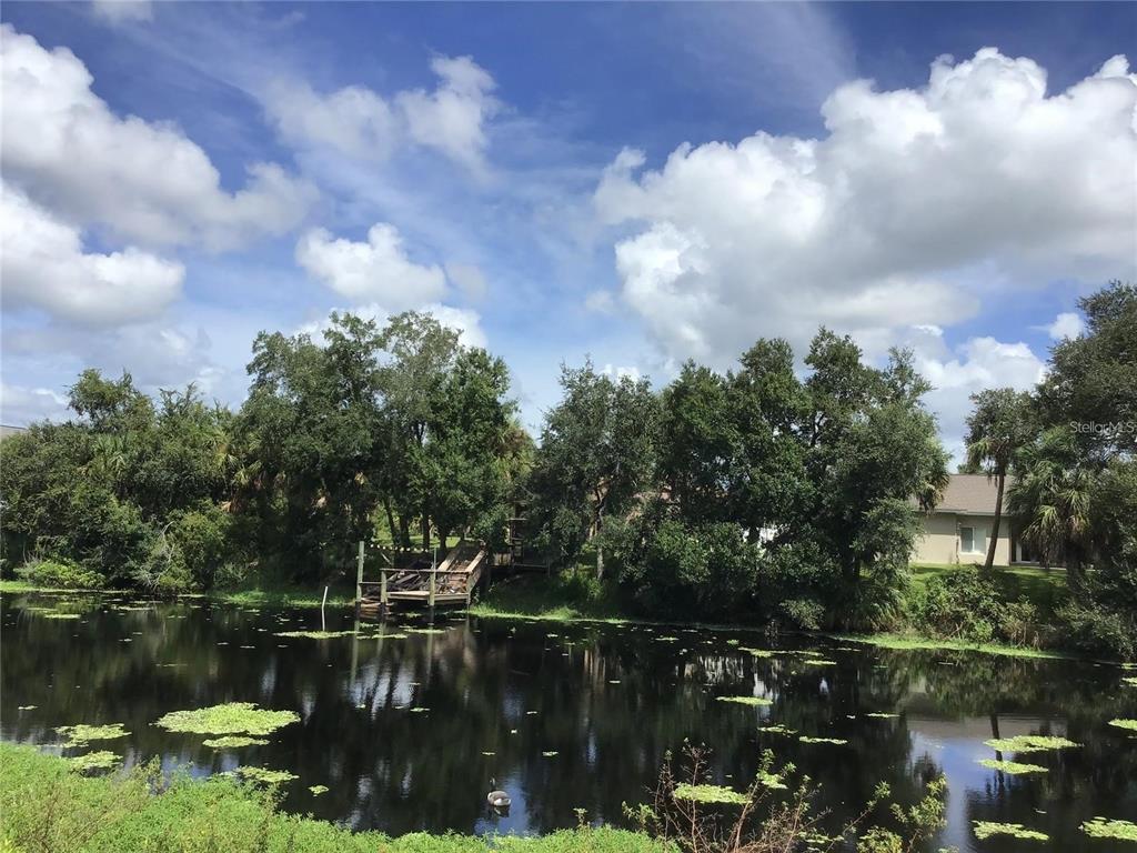 A wooden dock sits on the edge of a pond surrounded by trees and vegetation — 1292 W HILLSBOROUGH BOULEVARD, NORTH PORT, FL