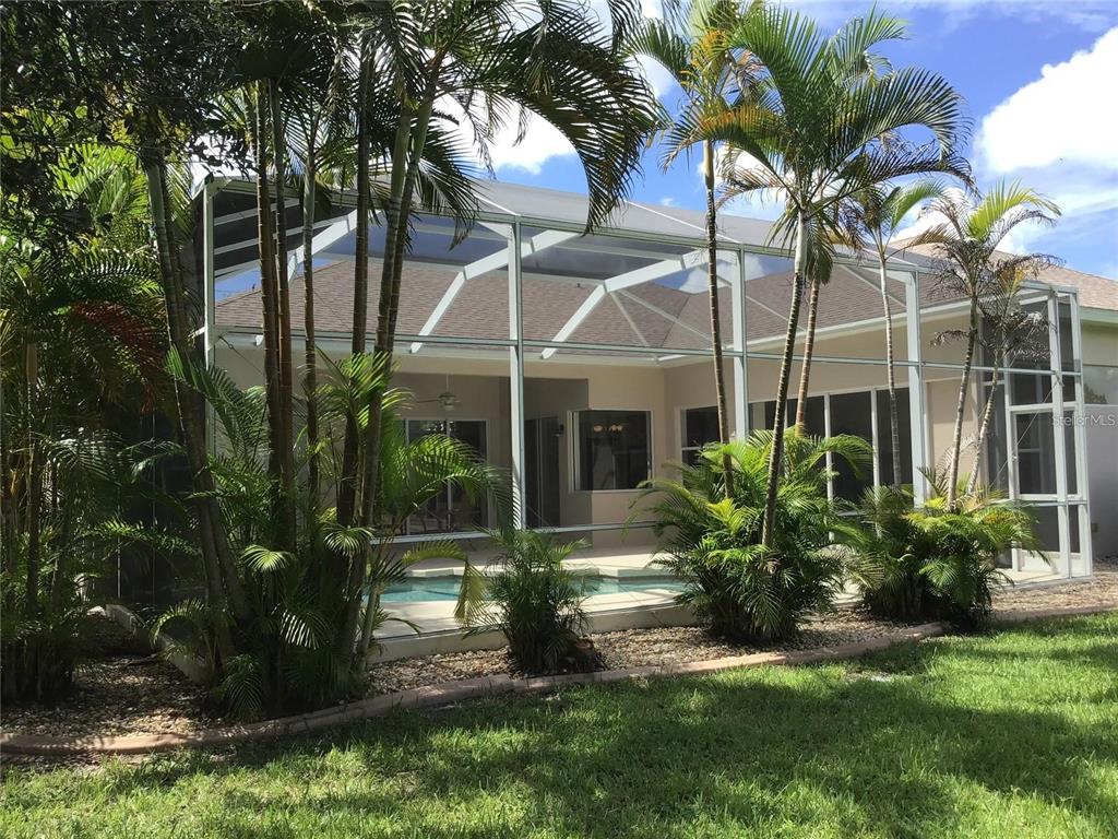 A screened-in pool patio with palm trees and a view of the house exterior — 1292 W HILLSBOROUGH BOULEVARD, NORTH PORT, FL