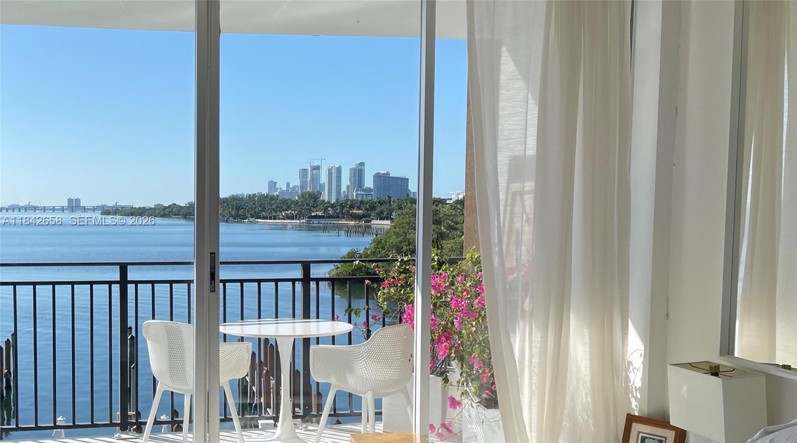 A balcony with two white wicker chairs overlooks a bay with a distant city skyline — 770 NE 69th St # 4H, Miami FL 33138, MIAMI, FL