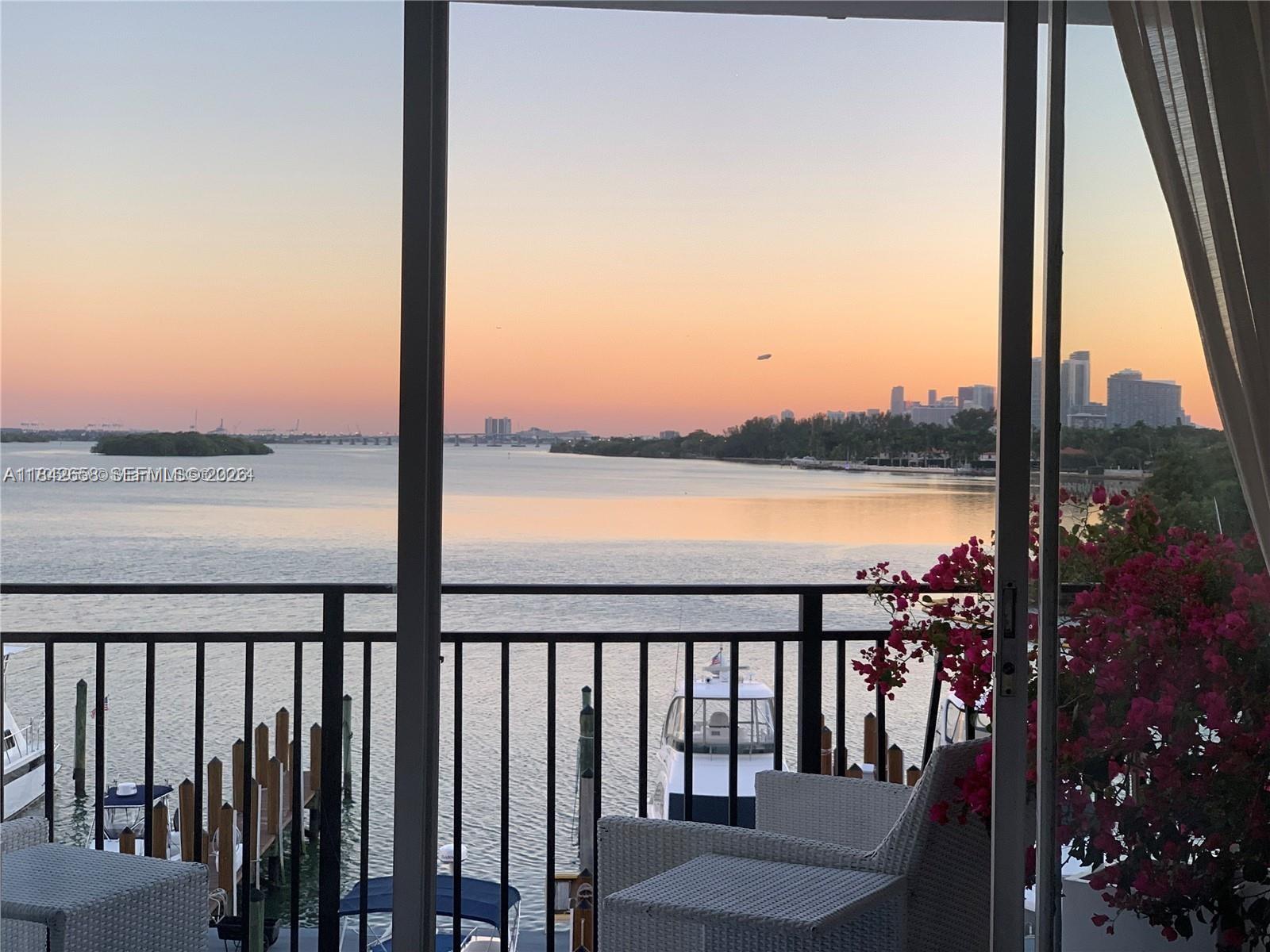 A balcony with white wicker chairs overlooks a bay with boats and a city skyline — 770 NE 69th St # 4H, Miami FL 33138, MIAMI, FL