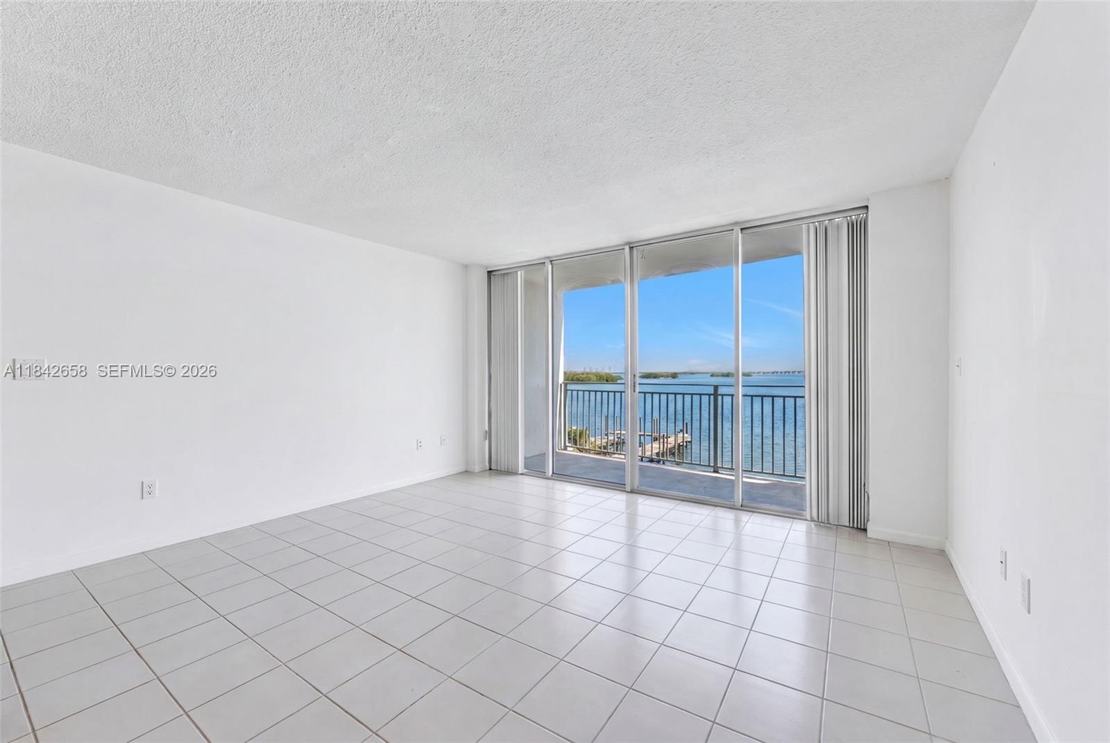 An empty room with white walls, tiled floors, and a sliding glass door overlooking water — 770 NE 69th St # 4H, Miami FL 33138, MIAMI, FL