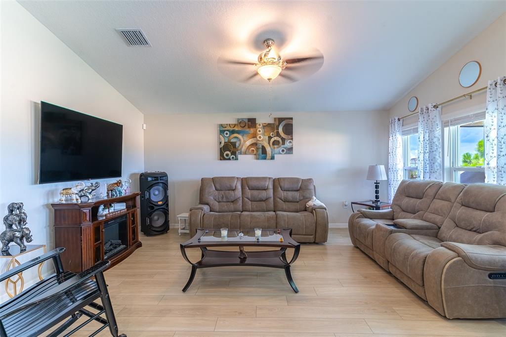A living room features light wood-look flooring, a brown sofa, a loveseat, and a television — 3704 DUSTY MILLER PLACE, HAINES CITY, FL