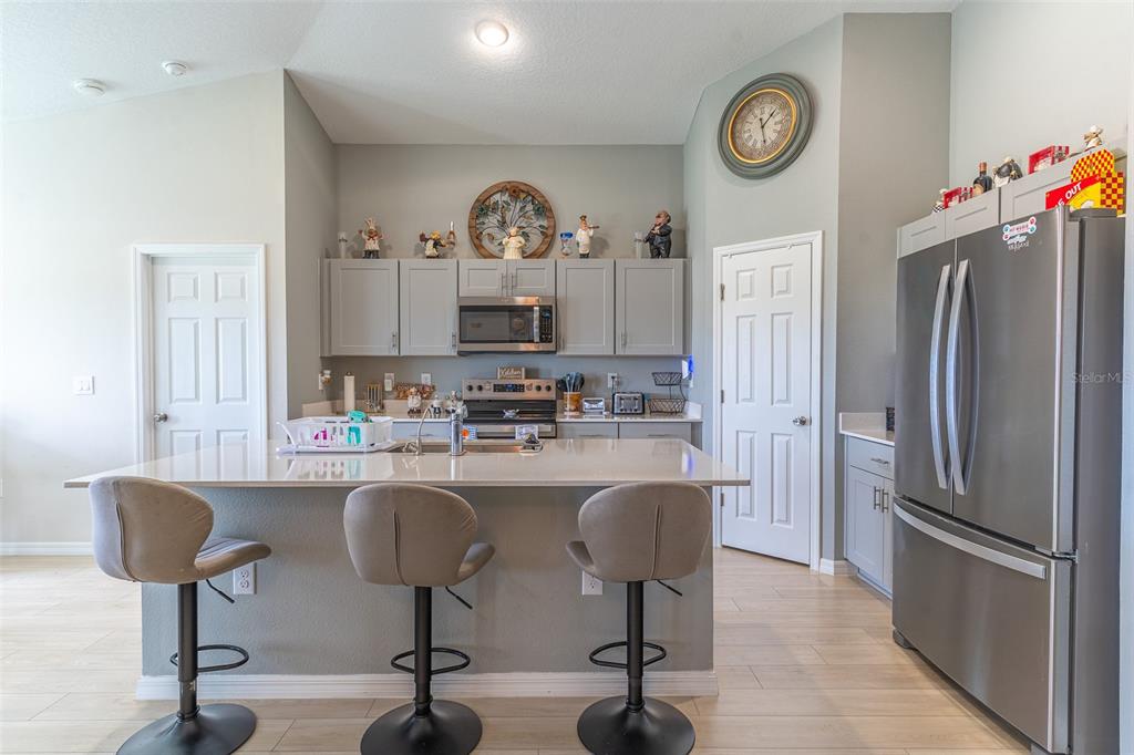 A kitchen features a central island with bar stools, stainless steel appliances, and gray cabinetry — 3704 DUSTY MILLER PLACE, HAINES CITY, FL
