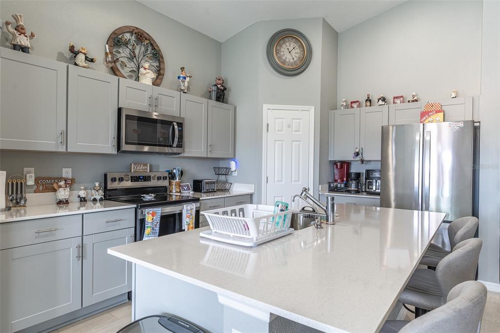 A modern kitchen features gray cabinets, stainless steel appliances, a large island, and quartz countertops — 3704 DUSTY MILLER PLACE, HAINES CITY, FL