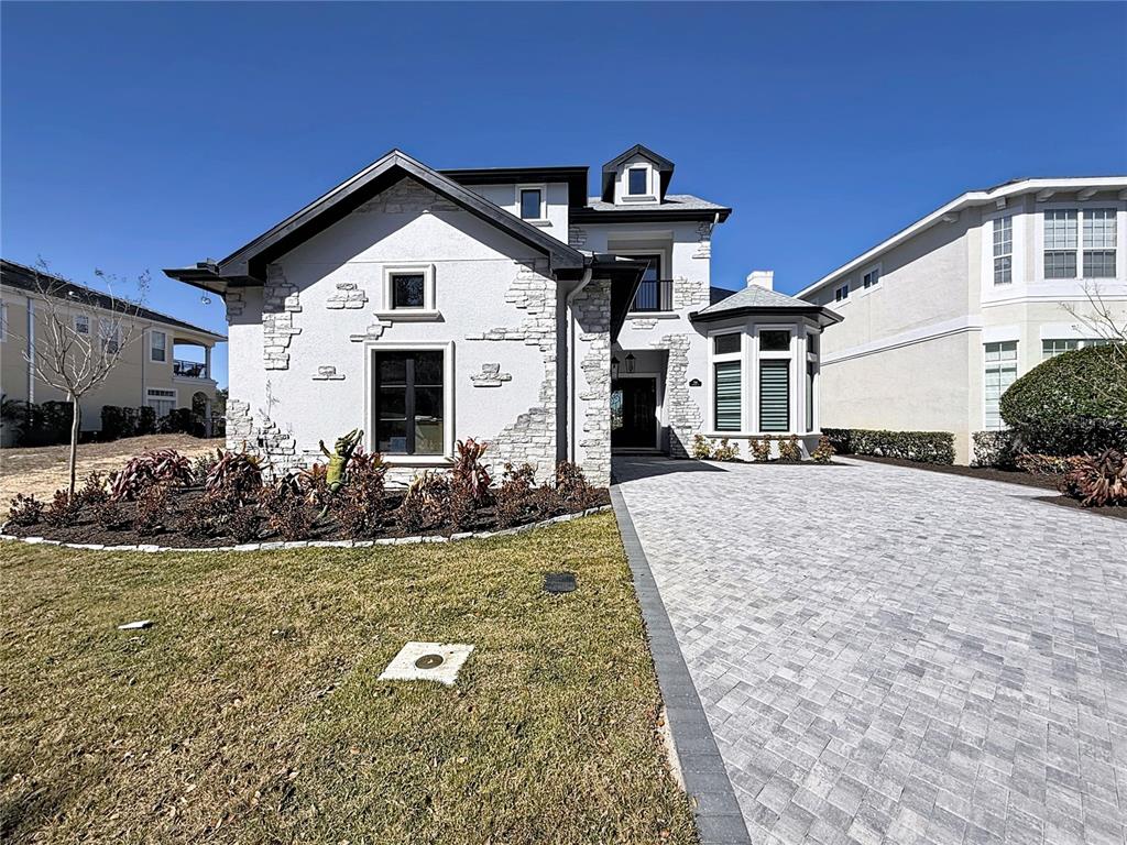 A two-story house with white stucco, stone accents, and a paved driveway under a blue sky — 7394 GATHERING COURT, REUNION, FL