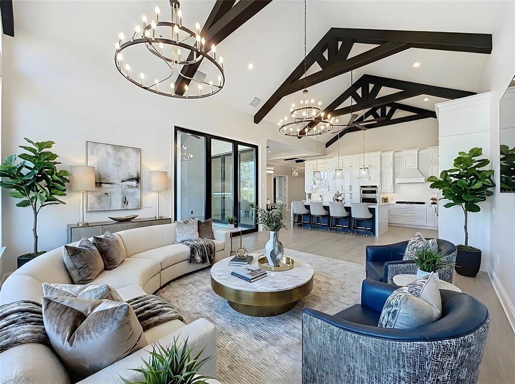 A living room with vaulted ceilings, exposed beams, chandeliers, a curved sofa, and open kitchen — 7394 GATHERING COURT, REUNION, FL