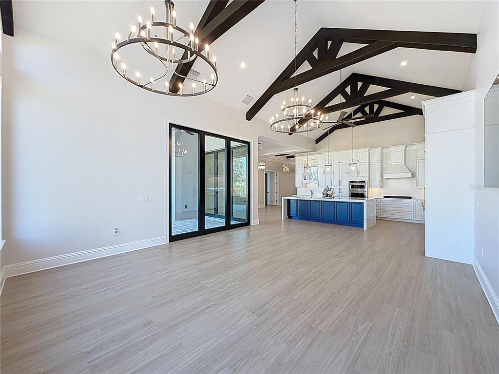 A spacious open-concept living area features vaulted ceilings with dark wooden beams and chandeliers — 7394 GATHERING COURT, REUNION, FL