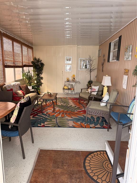 A sunroom features a patterned area rug, wicker furniture, and light-colored paneled walls — 38533 LANSING AVENUE, ZEPHYRHILLS, FL