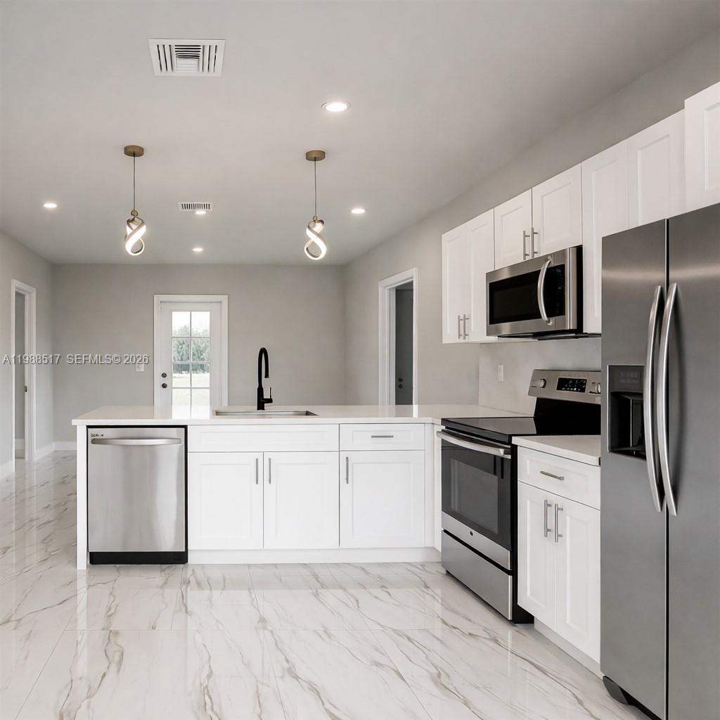A modern kitchen features white cabinetry, stainless steel appliances, and white marble-patterned tile flooring — 816 Palomino, Lehigh Acres FL 33974, LEHIGH ACRES, FL
