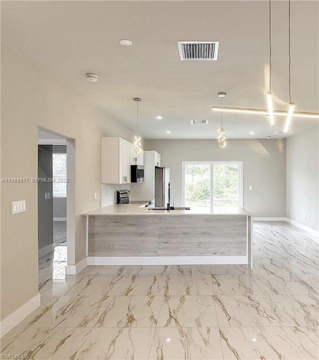 A modern kitchen features white cabinets, a wood-paneled island, and light-colored marble-patterned tile flooring — 816 Palomino, Lehigh Acres FL 33974, LEHIGH ACRES, FL
