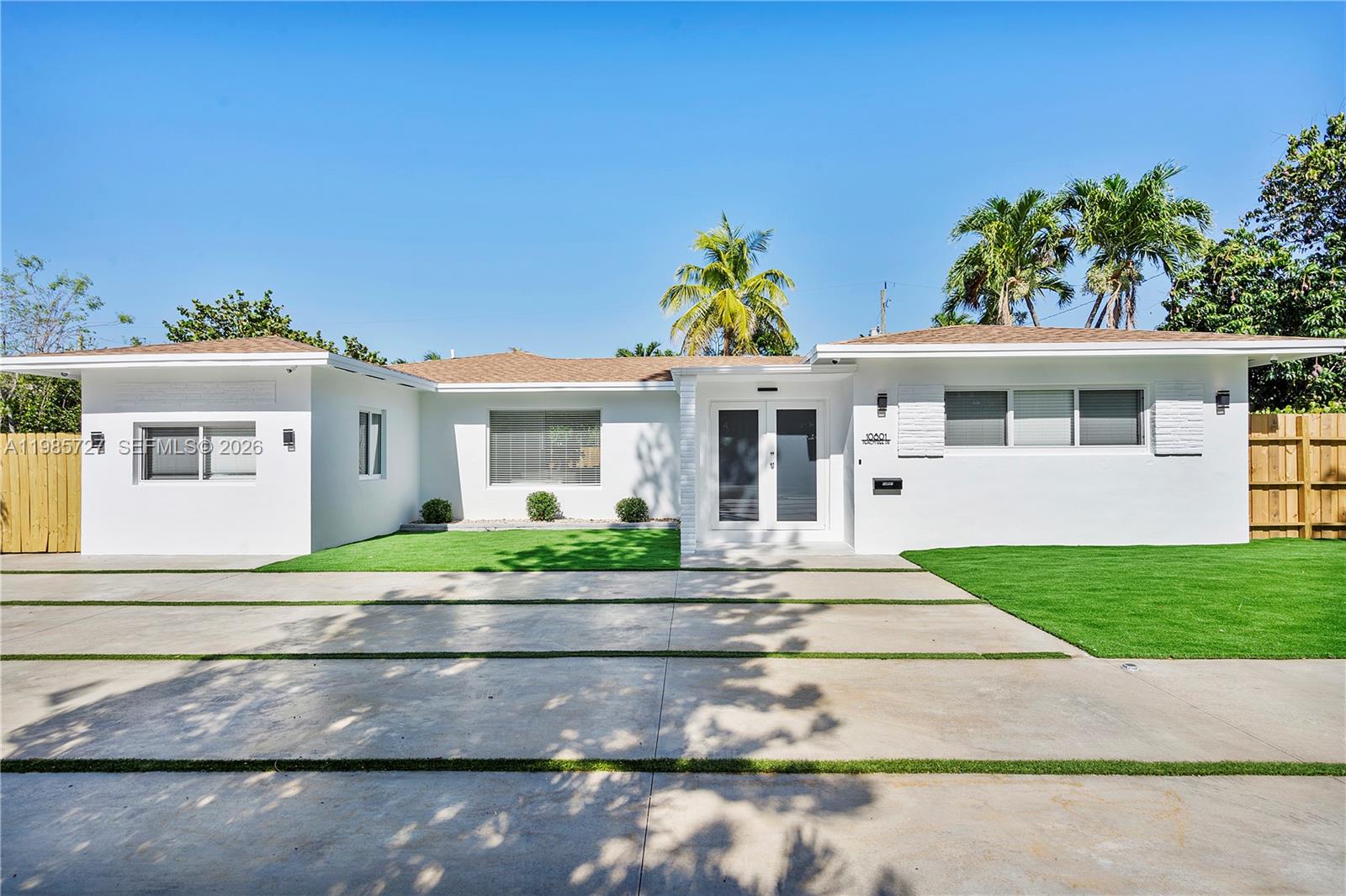 A white single-story house features a concrete driveway with grass strips and a front lawn — 10801 Peachtree Dr, Miami FL 33161, MIAMI, FL