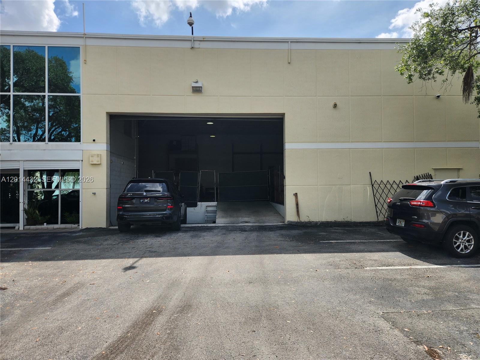 A commercial building exterior features a large loading bay and two parked SUVs — 8109 NW 29th St # 8109, Doral FL 33122, DORAL, FL