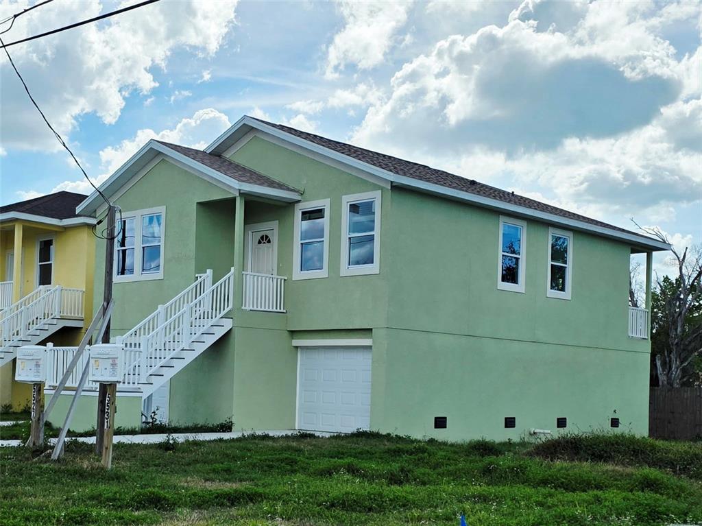 A light green elevated house features a white staircase, a garage door, and multiple windows — 5527 LEISURE LANE, NEW PORT RICHEY, FL