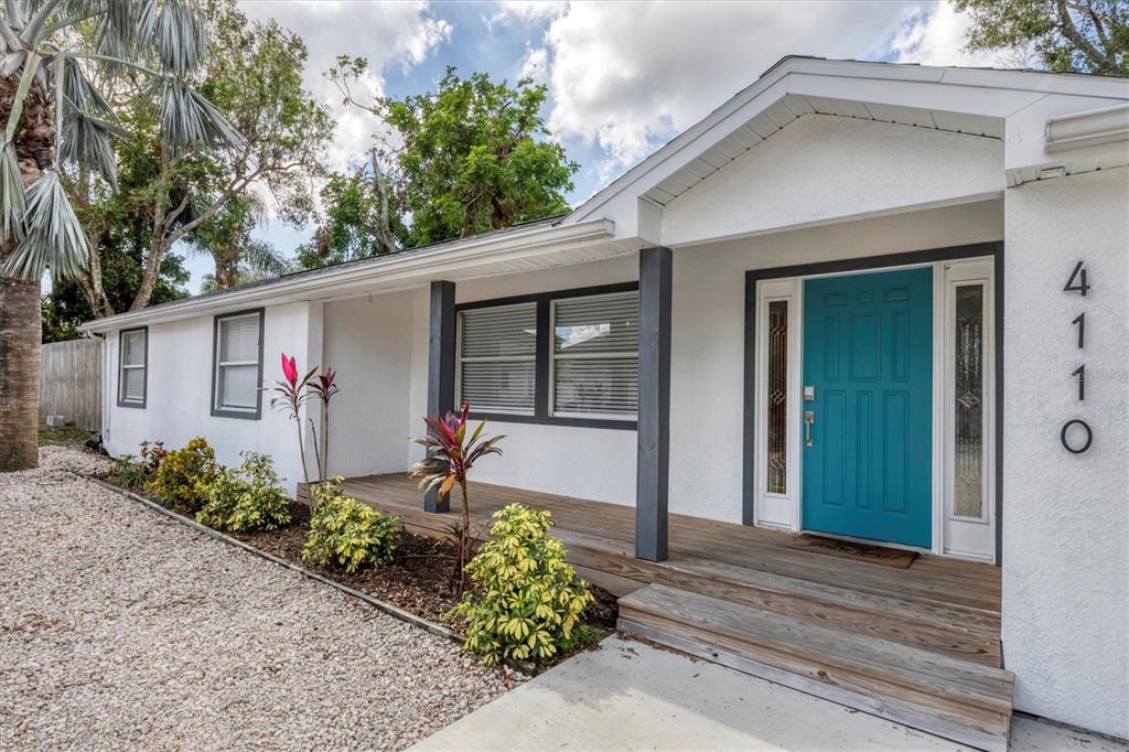 A white house exterior features a teal front door and a wooden porch — 4110 IOLA DRIVE, SARASOTA, FL