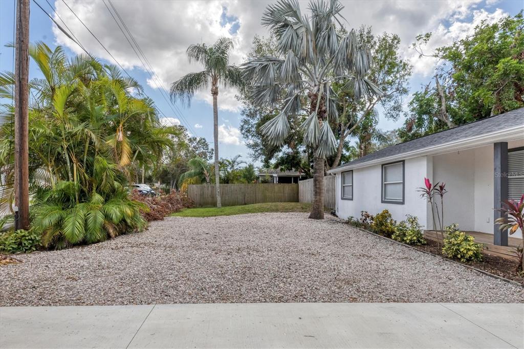 A gravel driveway leads to the side of a white house with palm trees — 4110 IOLA DRIVE, SARASOTA, FL