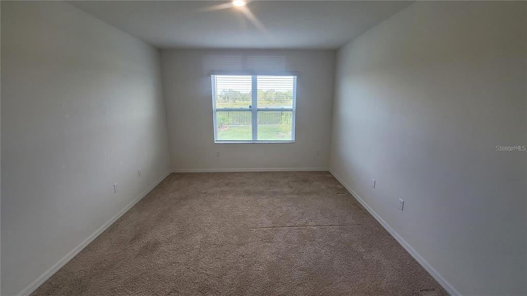 An empty bedroom with beige carpet, white walls, and a window overlooking a fenced yard — 1128 FOX PATH, DAVENPORT, FL