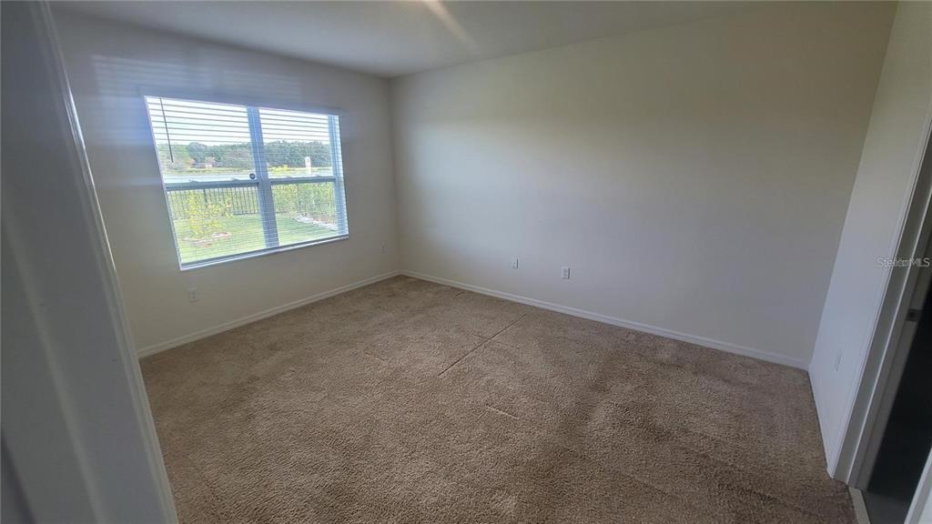 An empty bedroom features beige carpet, light-colored walls, and a window overlooking a grassy yard — 1128 FOX PATH, DAVENPORT, FL