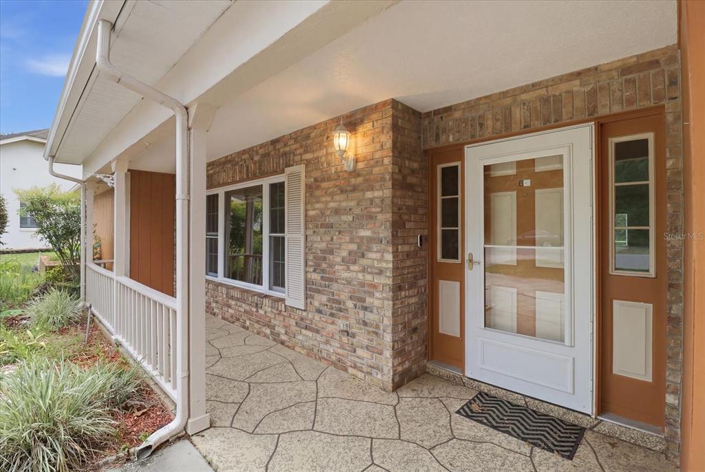 A covered porch with a brick exterior wall, a white front door, and patterned concrete flooring — 45 HOLLYHOCK COURT, HOMOSASSA, FL