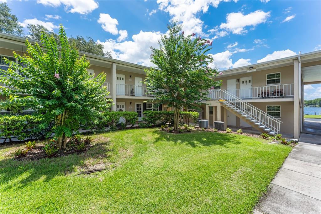 A two-story apartment building exterior features a grassy courtyard, mature trees, and an outdoor staircase — 2500 LEE ROAD UNIT 220, WINTER PARK, FL