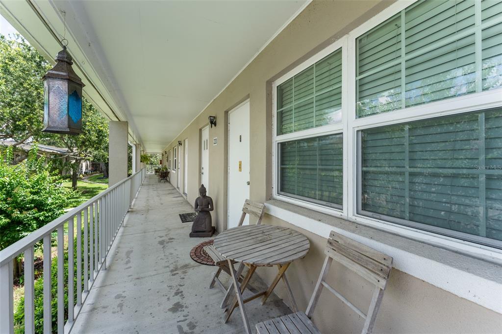 A covered outdoor walkway features a wooden table, chairs, and a decorative statue — 2500 LEE ROAD UNIT 220, WINTER PARK, FL