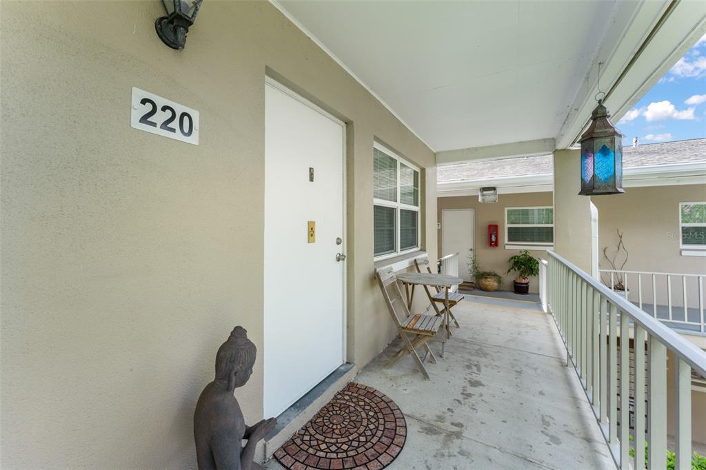 An outdoor apartment walkway features a white door labeled 220, a small table, and chairs — 2500 LEE ROAD UNIT 220, WINTER PARK, FL