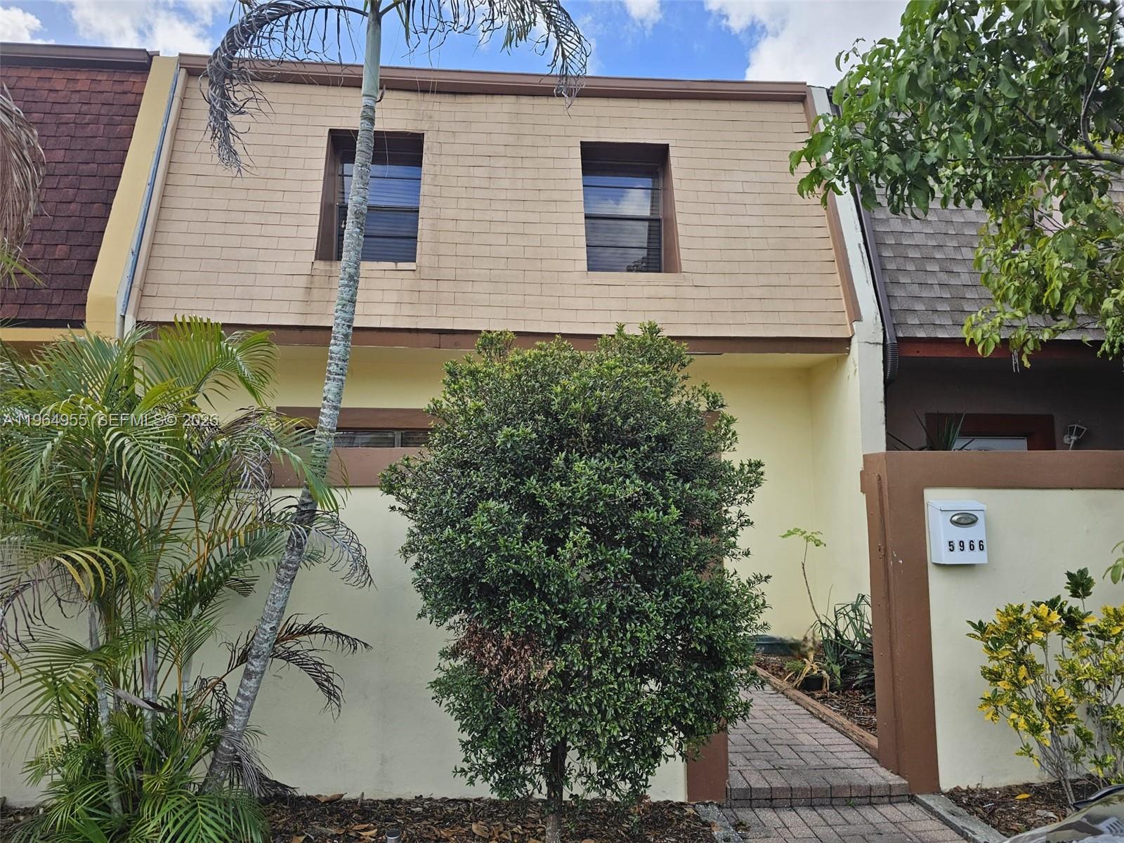 A two-story townhouse exterior features a tan shingled mansard roof, light yellow walls, and landscaping — 5966 NW 24th Ct, Sunrise FL 33313, SUNRISE, FL