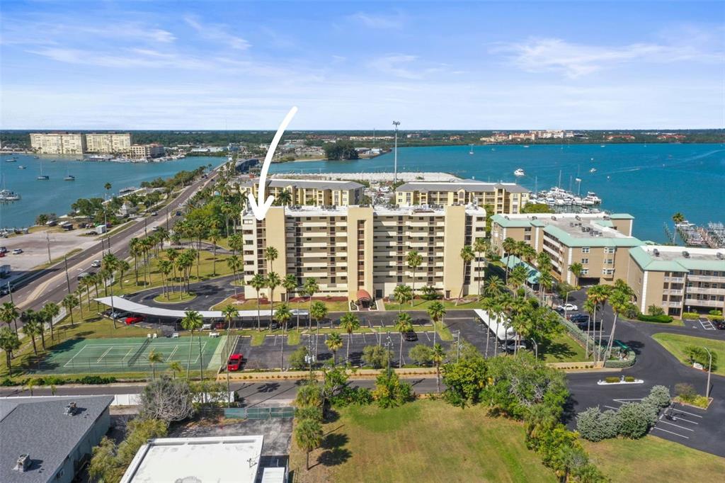An aerial view shows a multi-story apartment building with a tennis court and parking lot — 401 150TH AVENUE UNIT 241, MADEIRA BEACH, FL