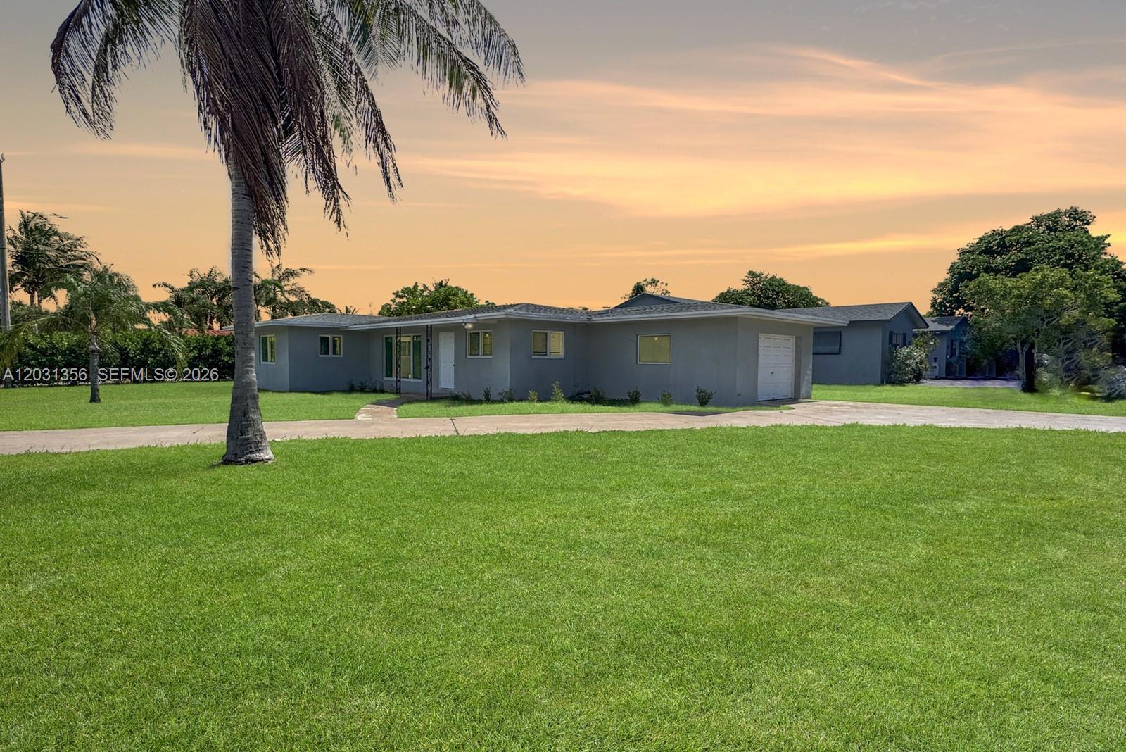 A gray single-story house with a garage sits on a large lawn at sunset — 231 NE 16th Ave, Pompano Beach FL 33060, POMPANO BEACH, FL
