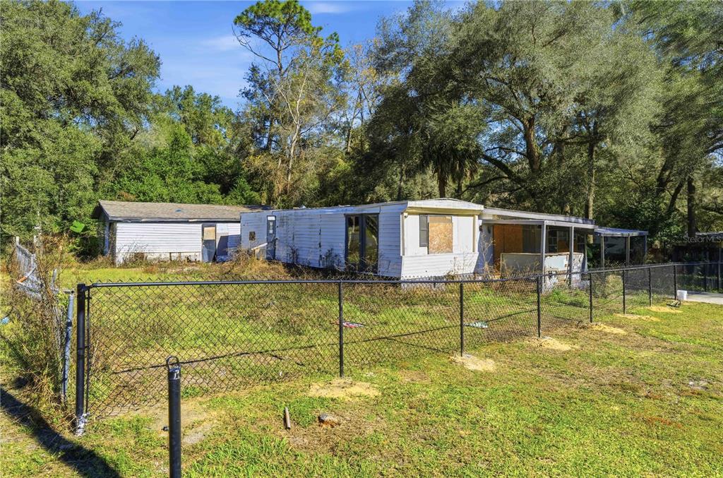 A weathered mobile home with a fenced yard sits on a lot surrounded by trees — 4265 S ILLIANA TERRACE, INVERNESS, FL