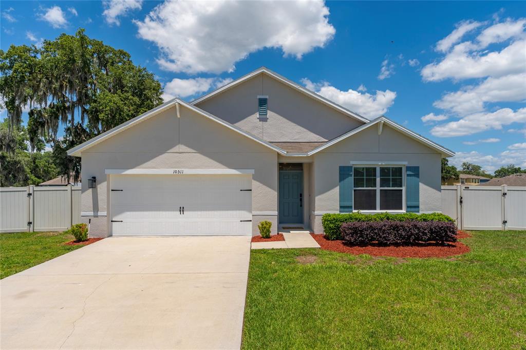 A single-story house with a white garage, blue shutters, and a light-colored stucco exterior — 10511 BURLWOOD DRIVE, LEESBURG, FL