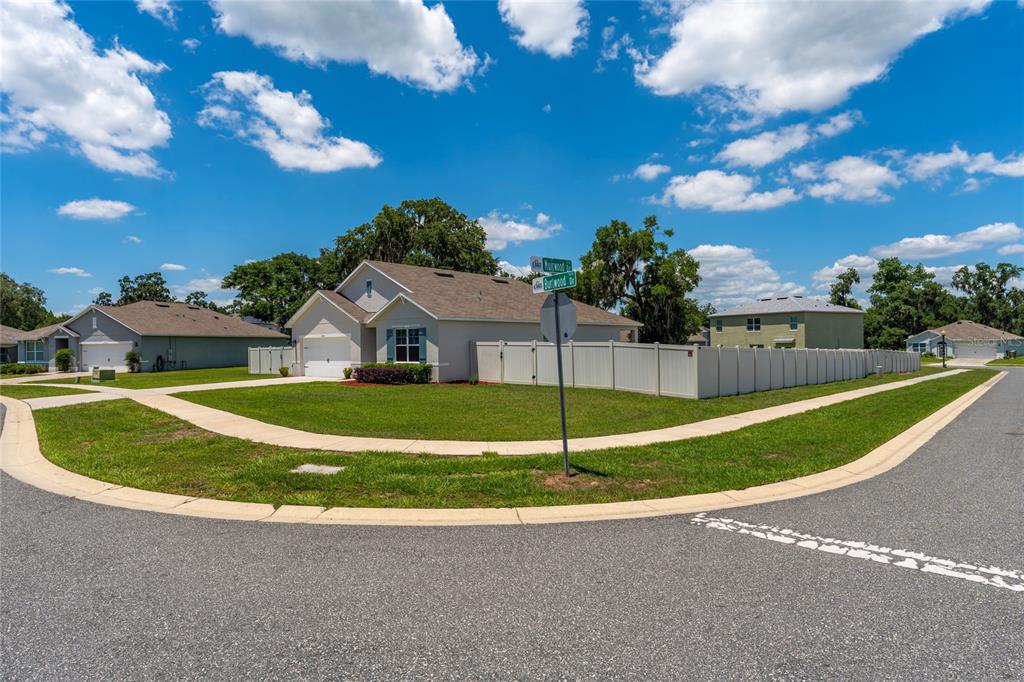 A single-story house with a white fence sits on a corner lot under a blue sky — 10511 BURLWOOD DRIVE, LEESBURG, FL
