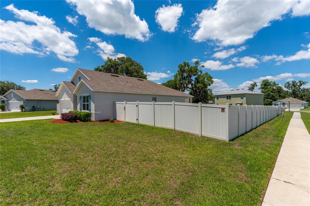 A light-colored house with a vinyl privacy fence stands on a grassy corner lot — 10511 BURLWOOD DRIVE, LEESBURG, FL