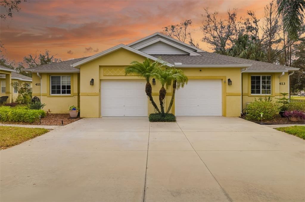 A yellow duplex with two white garage doors and a palm tree in the driveway — 411 28TH STREET W, PALMETTO, FL