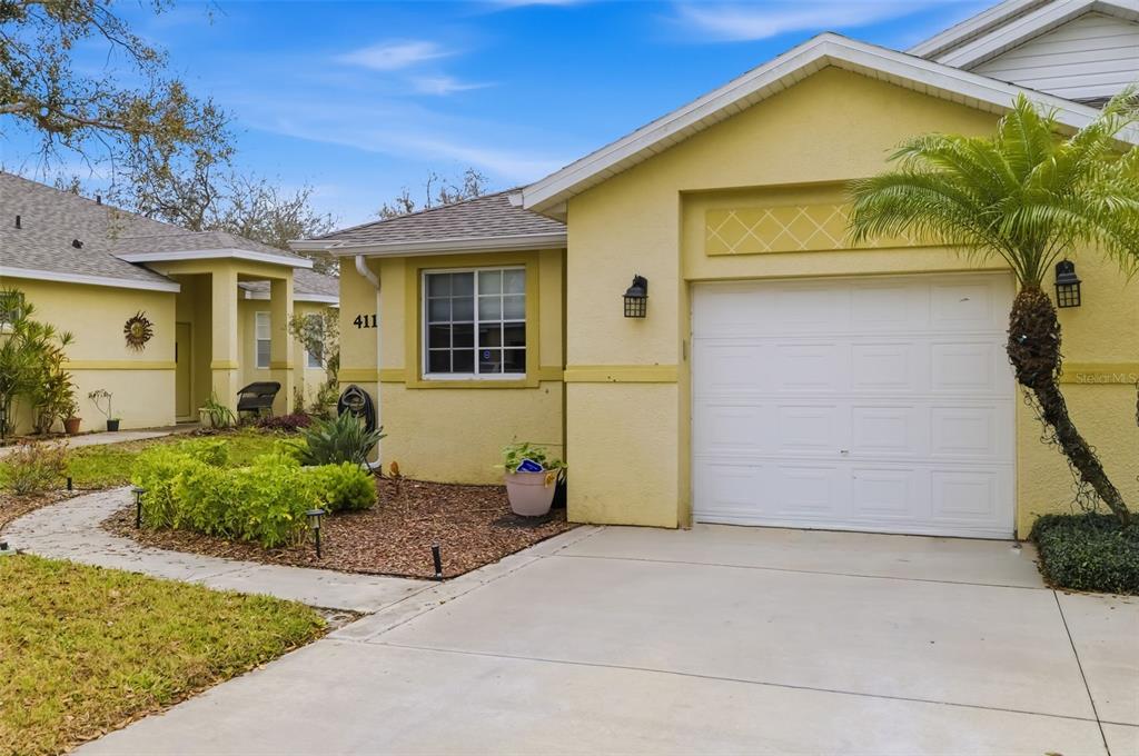 A yellow single-story house with a white garage door and a concrete driveway — 411 28TH STREET W, PALMETTO, FL