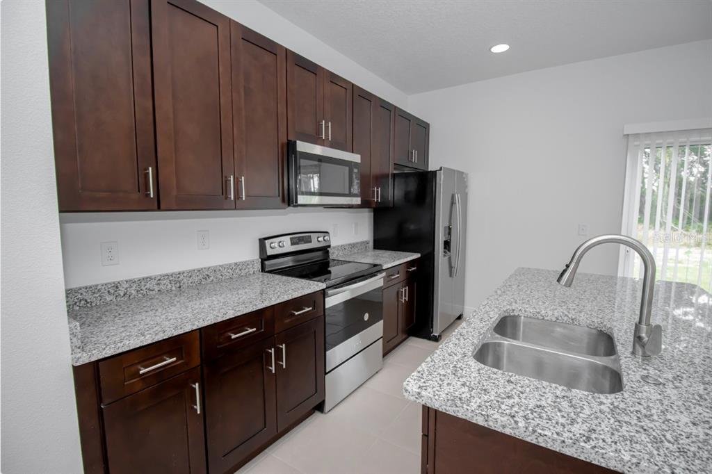 A kitchen with dark wood cabinets, granite countertops, stainless steel appliances, and a center island — 14587 SW 25TH TER, OCALA, FL 34473, OCALA, FL