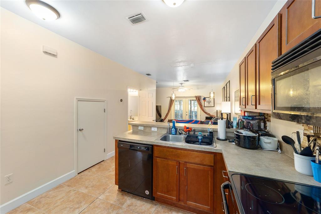 A kitchen with wood cabinets, a dishwasher, and a sink overlooks a living area — 2915 SW 35TH PLACE UNIT 102, GAINESVILLE, FL