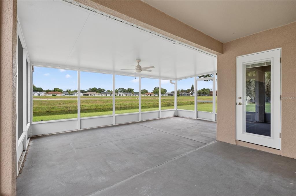 A covered, screened-in concrete patio overlooks a grassy lawn and a small canal — 5405 WATERVISTA DRIVE, ORLANDO, FL