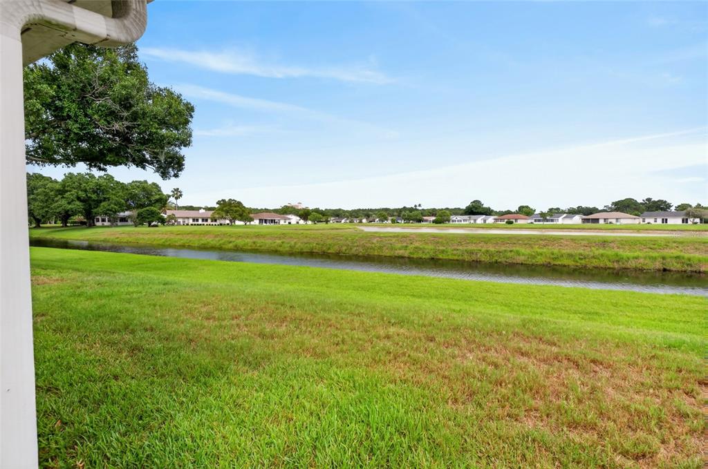 A view of a grassy lawn, a narrow canal, and distant houses under a blue sky — 5405 WATERVISTA DRIVE, ORLANDO, FL