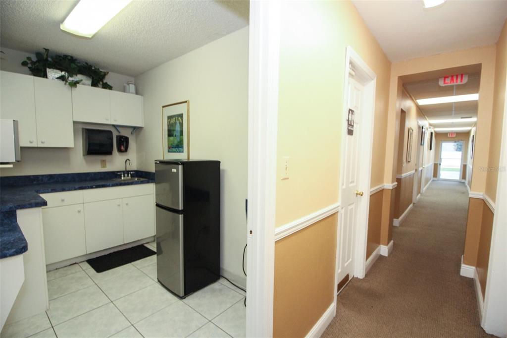 A small kitchenette with white cabinets and a black refrigerator sits beside a carpeted hallway — 407 LAKE HOWELL ROAD, MAITLAND, FL