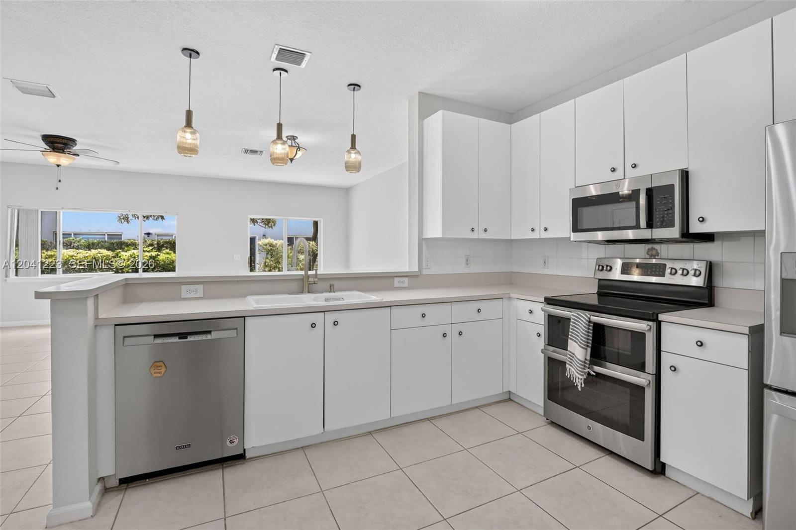 A kitchen with white cabinets, stainless steel appliances, and a pass-through window to the living area — 13212 NW 7th Dr, Plantation FL 33325, PLANTATION, FL