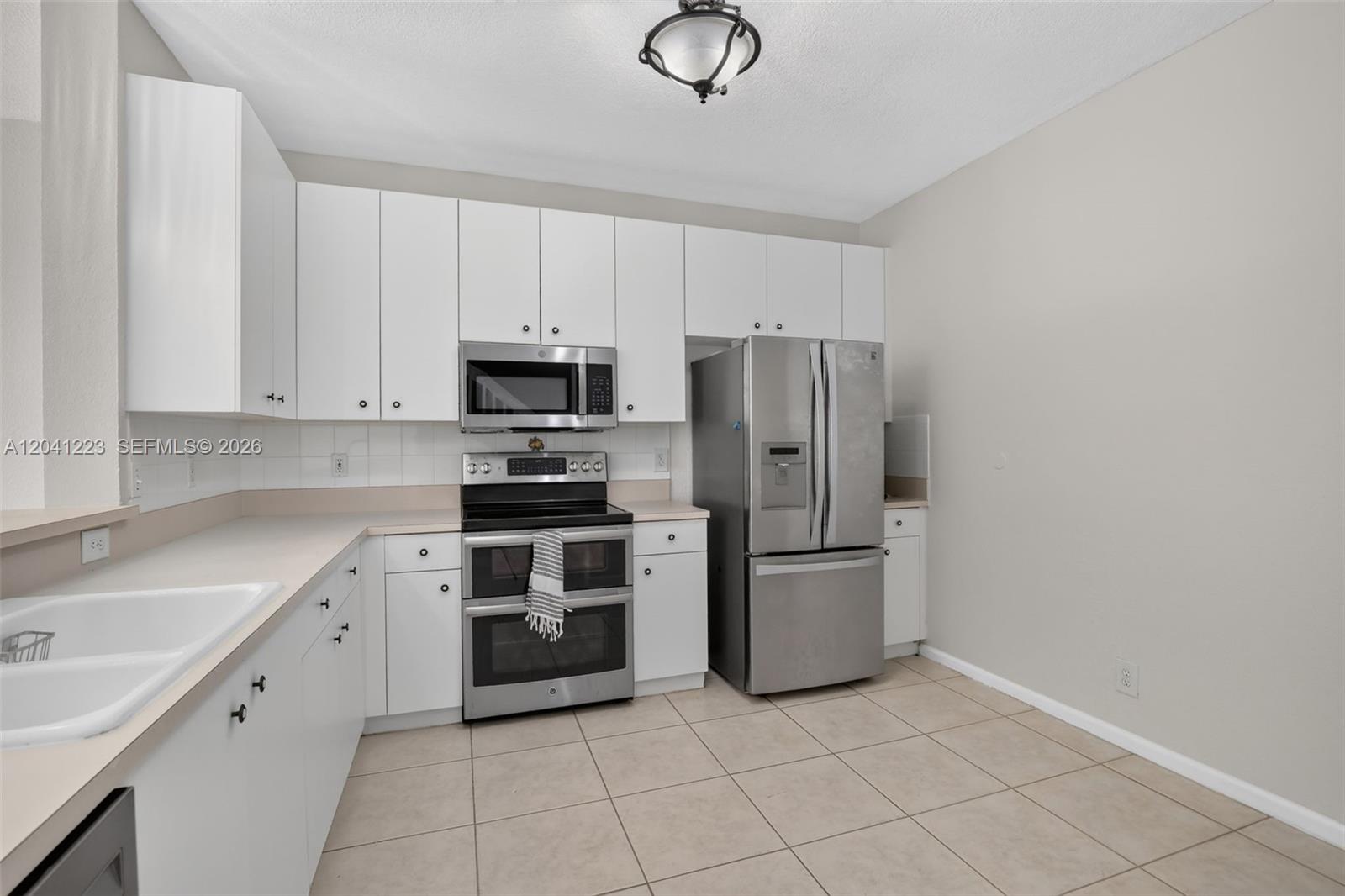 A kitchen features white cabinets, stainless steel appliances, a tiled floor, and beige countertops — 13212 NW 7th Dr, Plantation FL 33325, PLANTATION, FL