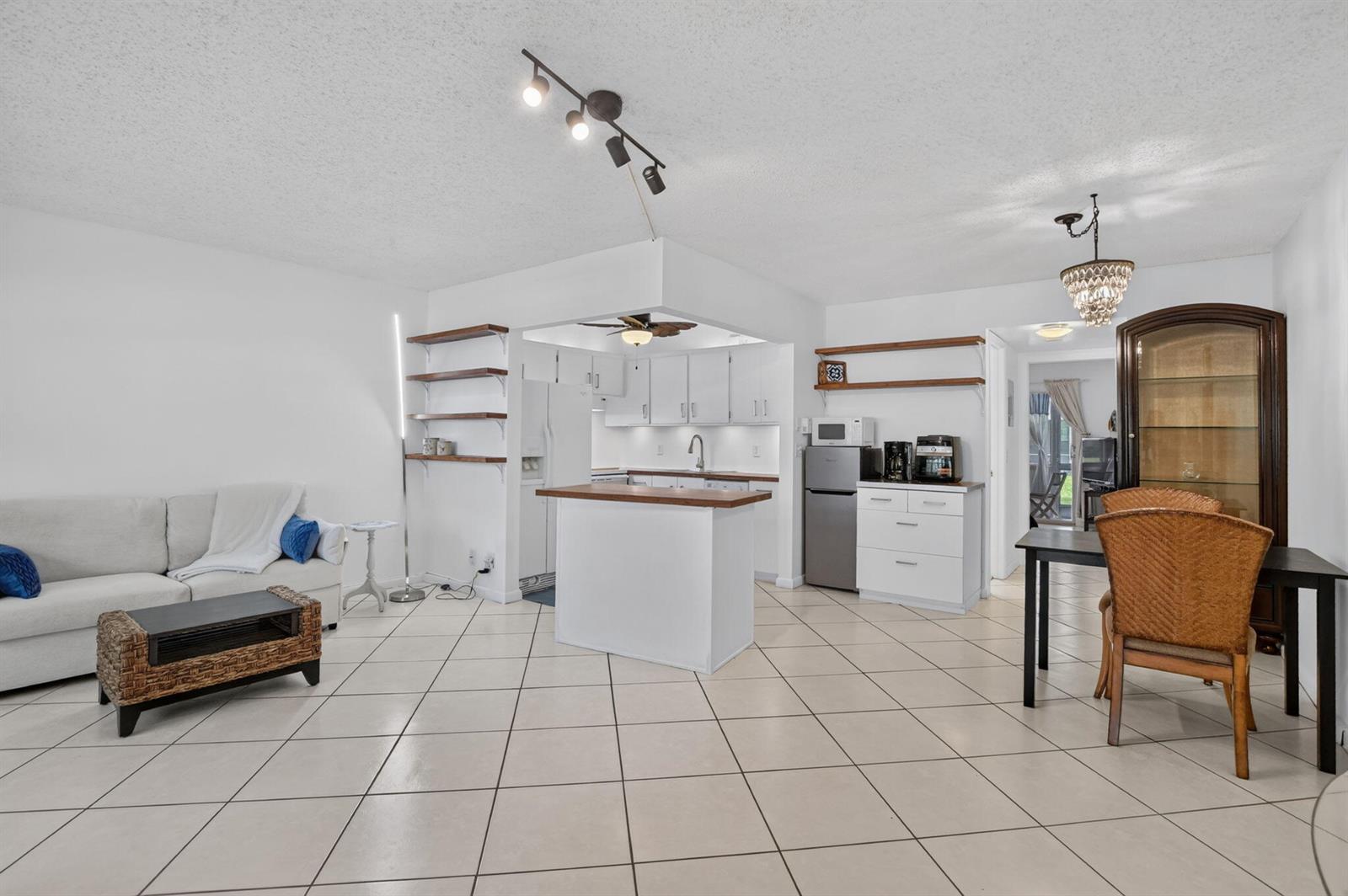 An open-concept living and dining area features white cabinets, tile flooring, and a kitchen island — 290 OAKRIDGE Q # 290, Deerfield Beach FL 33442, DEERFIELD BEACH, FL